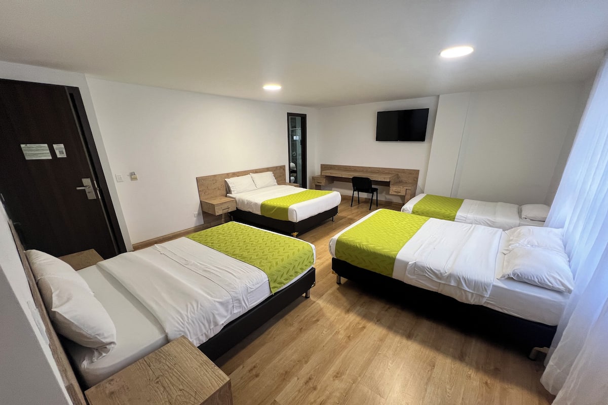 A hotel room with three beds, a desk, a chair, and a TV on the wall.