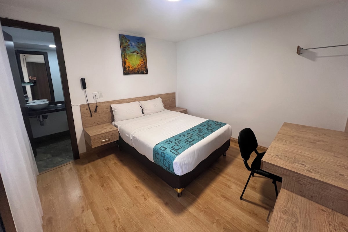 A bedroom with a bed, bedside table, and a desk.
