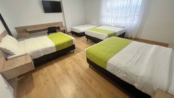 Habitación de hotel con dos camas individuales, un escritorio, una silla, un televisor y una ventana con cortinas.