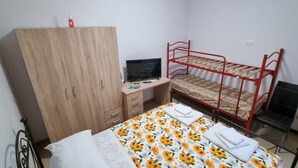 A bedroom with a bunk bed, a wooden wardrobe, a desk with a computer, and a bed with a floral bedspread.