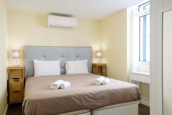 A hotel room with a bed, bedside tables, an air conditioner, and a window.