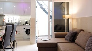 Ein modernes Wohnzimmer mit einer Couch und Sesseln, ein Essbereich mit Tisch und Stühlen sowie eine Küche mit Geräte.