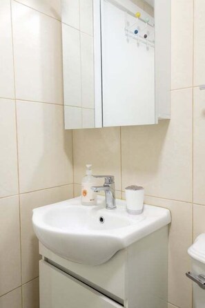 Et badeværelse med hvid vask, spejl og toilet.
