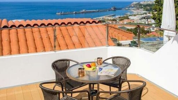 Eine Terrasse mit Tisch und Stühlen, mit Blick auf die Küste, Gebäude und einen Steg.