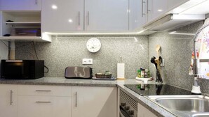 Eine moderne Küche mit weißen Schränken, einer Arbeitsplatte aus Granit, einer Mikrowelle, einem Toaster, einer Spüle und einer Uhr.