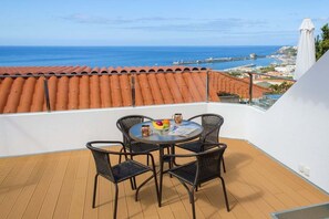 Et rundt bord med fire stole på en balkon med udsigt til havet og en bro.