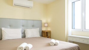 Ein Hotelzimmer mit einem Bett, zwei Kissen, einem Nachttisch mit Lampe und einem fenster mit Vorhängen.
