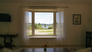 Ett rum med ett stort fönster, ett litet bord med en vas och en inramad tavla på väggen.