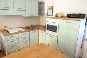 A compact kitchen with light green cabinets, a wooden countertop, a white stove, and a radio on the counter.