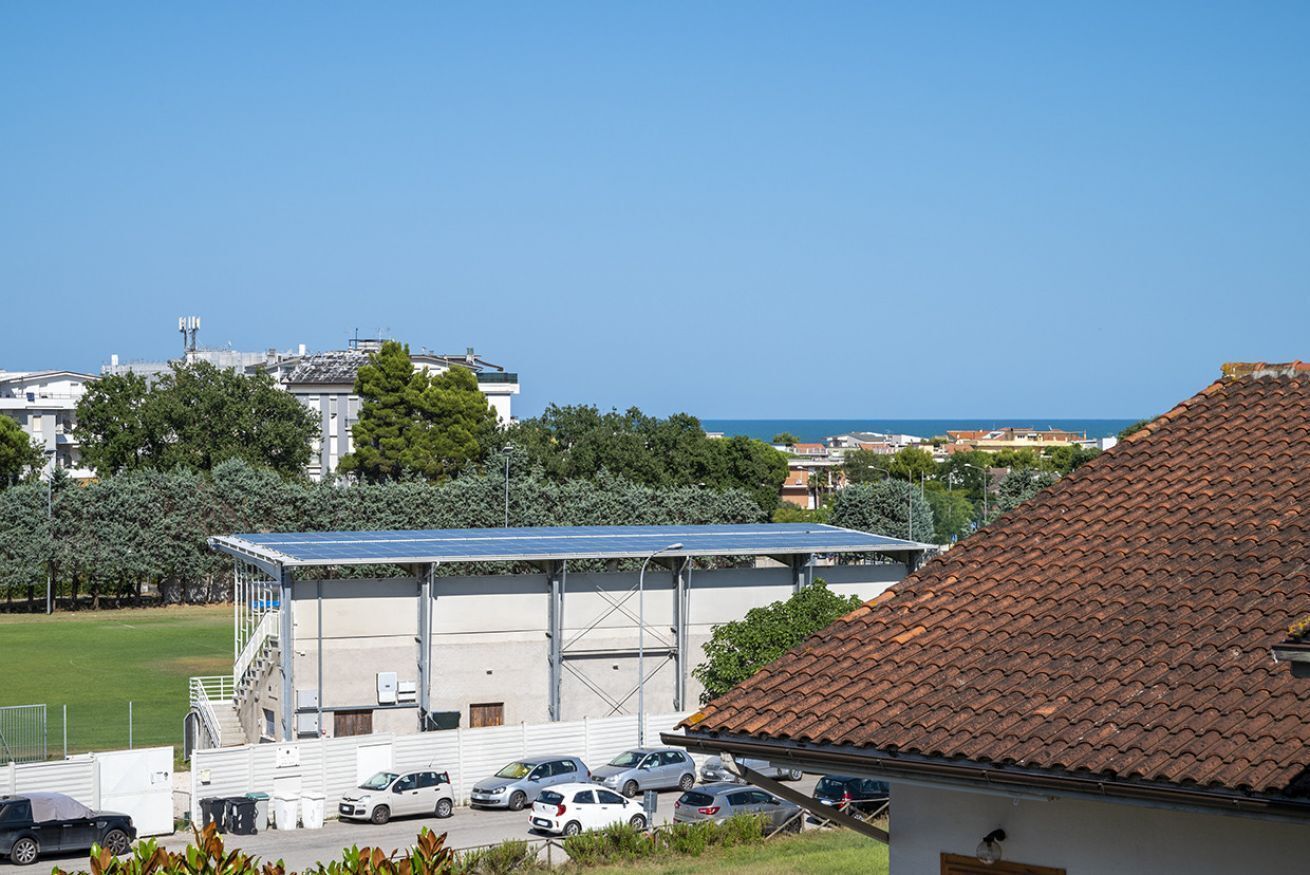 A building with a covered outdoor area, parked cars, and a view of the sea.