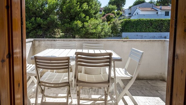 Eine Terrasse im Freien mit Tisch und Stühlen, Blick auf Bäume und Häuser sowie ein hölzerner Türrahmen.