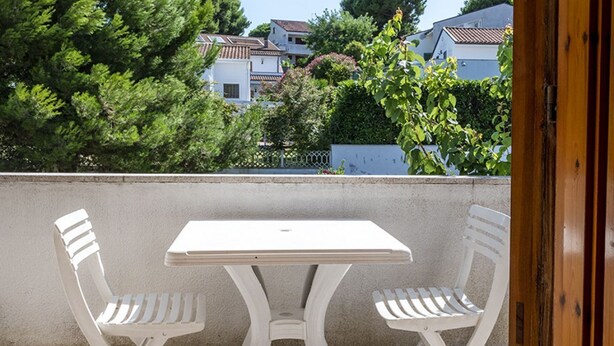 Een balkon met een witte tafel en twee witte stoelen, met uitzicht op een woonwijk met huizen en bomen.