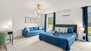 A modern bedroom with a large bed, a blue sofa, and a small table with a lamp. - Hot tub, Fire-pit, Pool Table, Heated Pool (Jamestown)