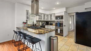 A modern kitchen with a central island, bar stools, stainless steel appliances, and a black refrigerator. - Hot tub, Fire-pit, Pool Table, Heated Pool (Jamestown)