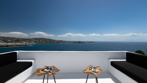 Ein Balkon mit zwei Holztischen, jeder Tisch gedeckt mit einer Tasse und einem Untertasse, mit Blick auf eine Küstenlandschaft, die Gebäude und das Meer zeigt.