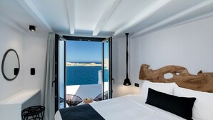 Ein modernes Schlafzimmer mit einem großen Bett, einem Holz-Kopfende, Meerblick und einem Balkon mit einem Stuhl.