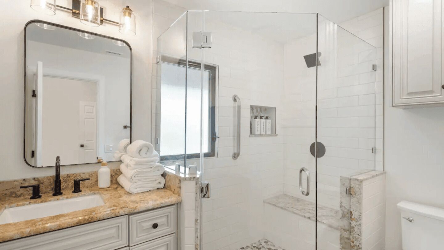 Un baño moderno con ducha de vidrio, lavamanos con encimera de mármol y un espejo grande.
