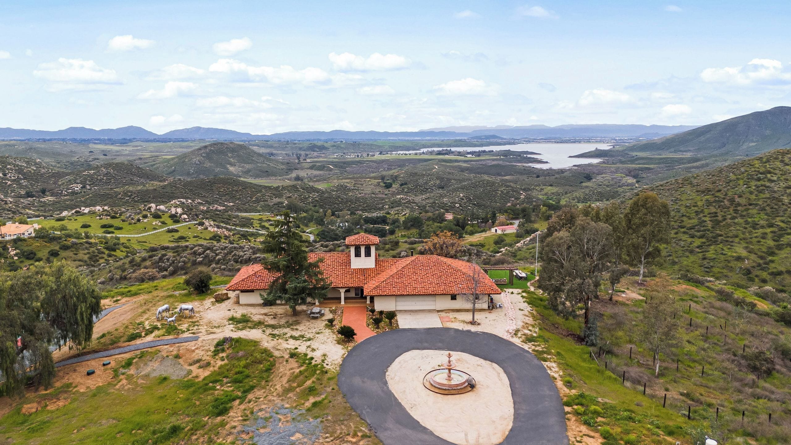 A villa with a red-tiled roof, surrounded by a landscaped garden and a view of a valley and mountains.