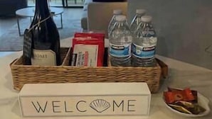 Une pancarte de bienvenue, une bouteille de vin, des bouteilles d’eau et une boîte de collations sont disposées sur une table.