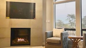 Un salon moderne avec une cheminée, un canapé et une grande fenêtre donnant sur la forêt.