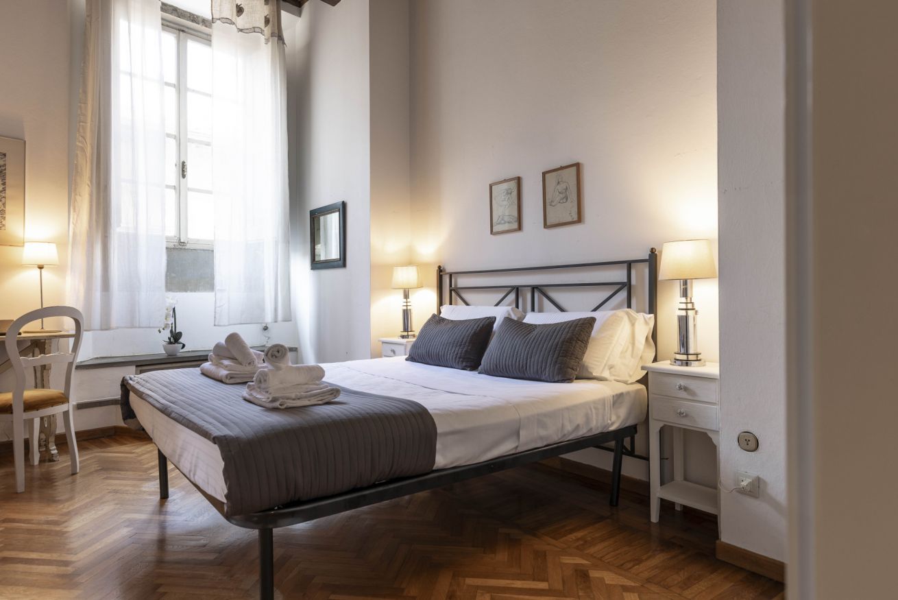 A neatly arranged bedroom with a bed, bedside tables, a chair, and a window with curtains.