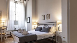 Ein ordentlich eingerichtetes Schlafzimmer mit Bett, Nachttischen, einem Sessel und einem Fenster mit Vorhängen.