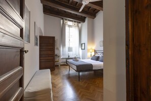 A bedroom with a wooden bed, a bench, a desk, and a window with curtains.