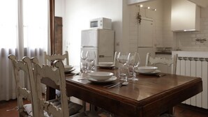 Ein Essbereich mit einem Holztisch, gedeckt für zwei Personen, weißen Stühlen und einem weißen Kühlschrank im Hintergrund.