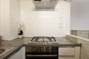 Una cocina con azulejos blancos tipo metro, una estufa a gas, electrodomésticos de acero inoxidable y una orquídea en maceta.