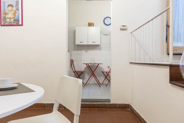 A small, compact kitchen with white cabinets, a red folding table, and a white chair.