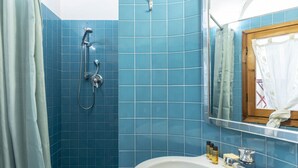 A bathroom with blue tiles, a shower, a sink with toiletries, and a mirror. - Casa Florentia - Florence (Firenze)