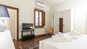 A hotel room with a bed, a TV, a wardrobe, a chair, and a window with open shutters. - Casa Florentia - Florence (Firenze)