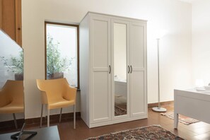 A room with a white wardrobe, a yellow chair, a small table, and a floor lamp.