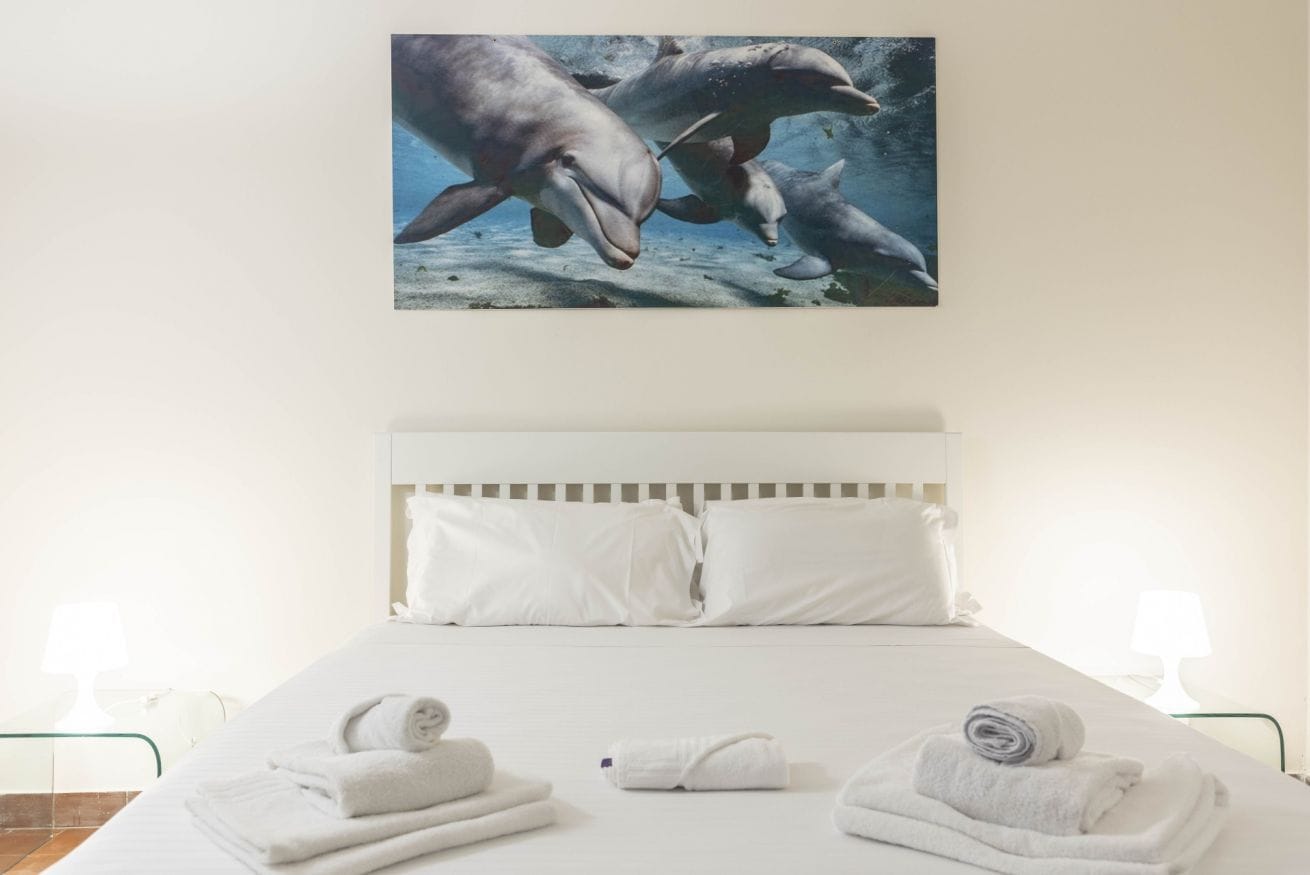A hotel room with a bed, white linens, and a painting of dolphins on the wall.