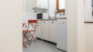A compact kitchen with white cabinets, a microwave, a sink, and a red folding chair. - Casa Florentia - Florence (Firenze)