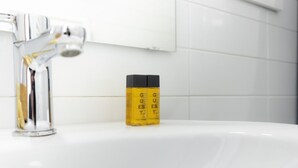 Um banheiro com pia branca, torneira cromada e uma garrafa amarela de shampoo.