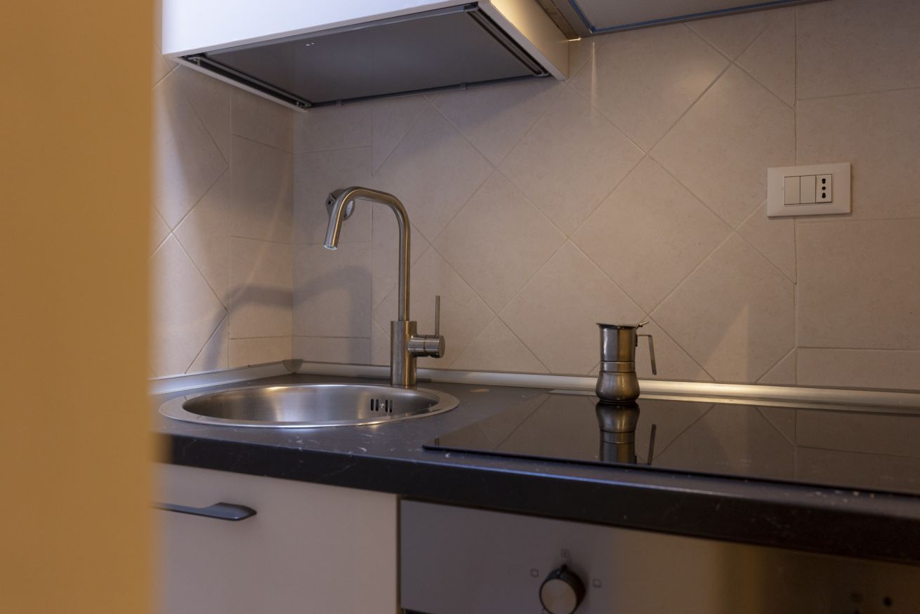Een keuken met een roestvrijstalen spoelbak, een moderne kraan en een compact koffiezetapparaat op het aanrecht.