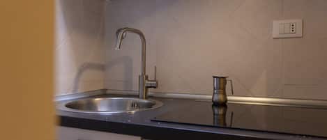 Een keuken met een roestvrijstalen spoelbak, een moderne kraan en een compact koffiezetapparaat op het aanrecht.