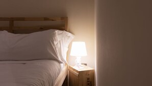 A bed with white bedding and a wooden headboard, a bedside table with a lamp, and a wall with a partial view of a door.
