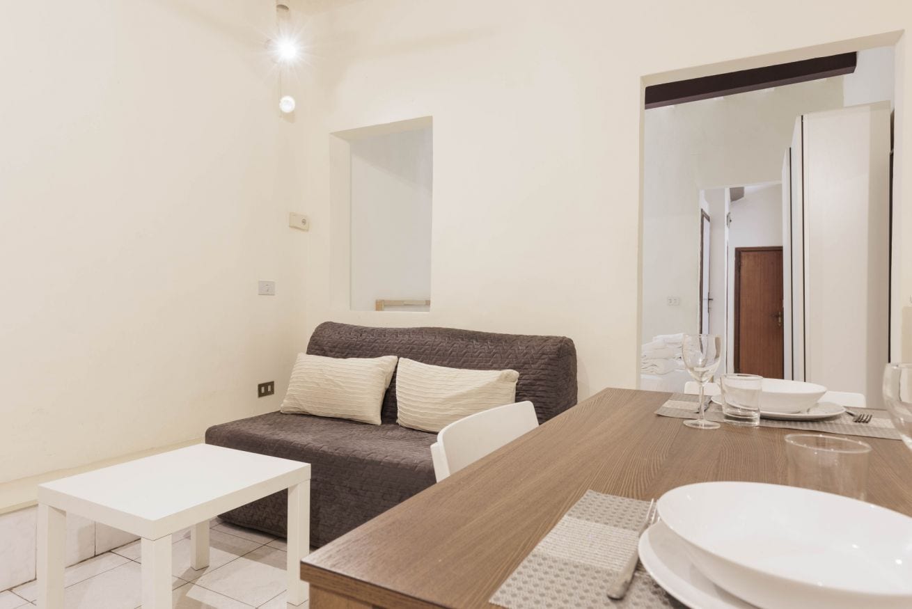 Ein modernes, helles Zimmer mit einem braunen Sofa, einem weißen Tisch und einem Essbereich mit einem Holztisch und weißen Tellern.