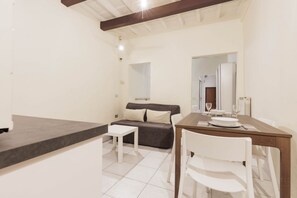 Une pièce moderne et bien éclairée, avec une table à manger, des chaises blanches, un canapé et une petite table blanche.