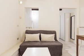 Une petite pièce moderne avec un canapé marron foncé, deux coussins blancs et une table blanche.