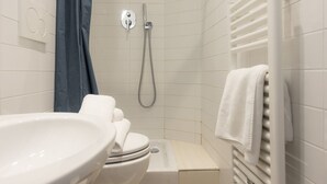 Un baño con lavamanos, inodoro y zona de ducha blanca.