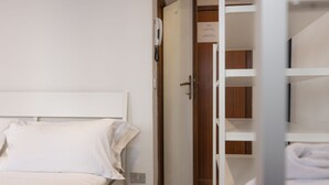 Una habitación de hotel con una cama, una puerta de madera y un armario blanco con estantes.