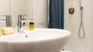 Un baño con lavamanos blanco, grifería cromada, espejo, ducha y toallero.
