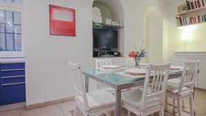 A dining area with a glass table, white chairs, a flat-screen TV mounted on the wall, and a bookshelf with books. - Duomo Deluxe Apartment (Firenze)