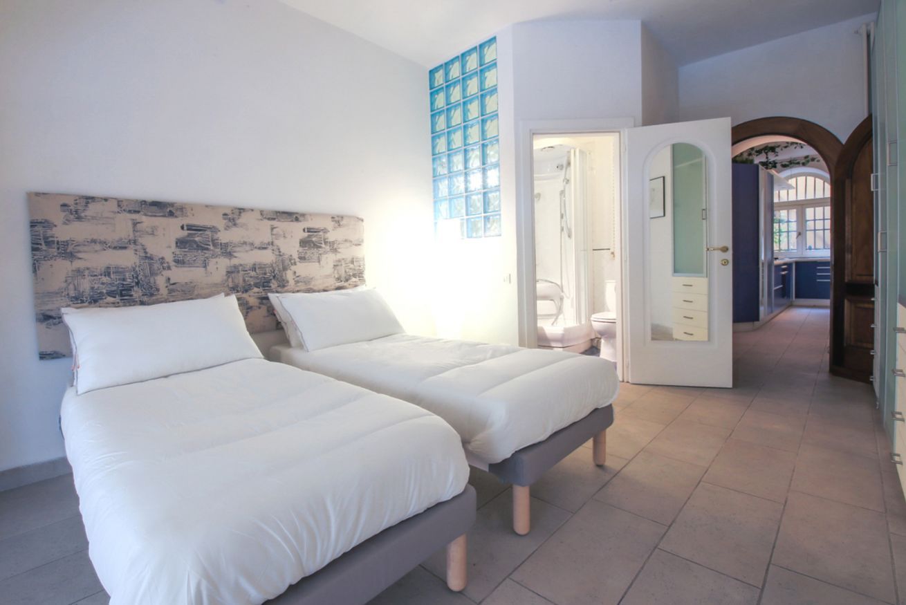 Un dormitorio con dos camas, un ventanal con vidrios azules y una puerta que da a otra habitación.