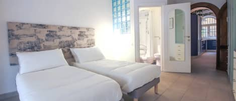 Un dormitorio con dos camas, un ventanal con vidrios azules y una puerta que da a otra habitación.