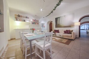 Una sala de estar moderna con comedor, muebles blancos y una estantería.