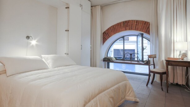 Una camera da letto con un letto grande, una scrivania e una vista attraverso una finestra ad arco in mattoni.